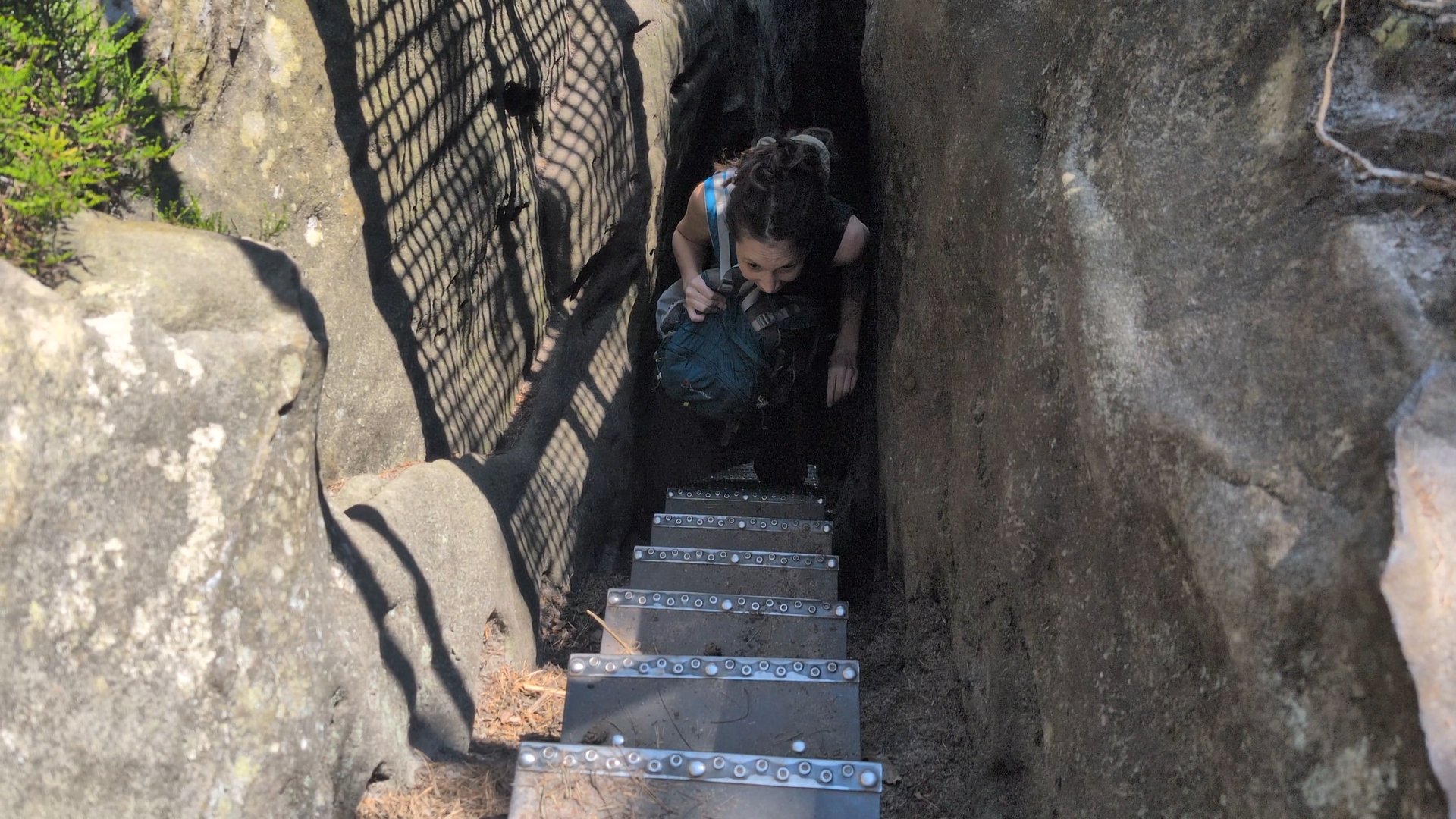 Kate climbing very steep stairs. She looks happy. Her backpack is on her front.