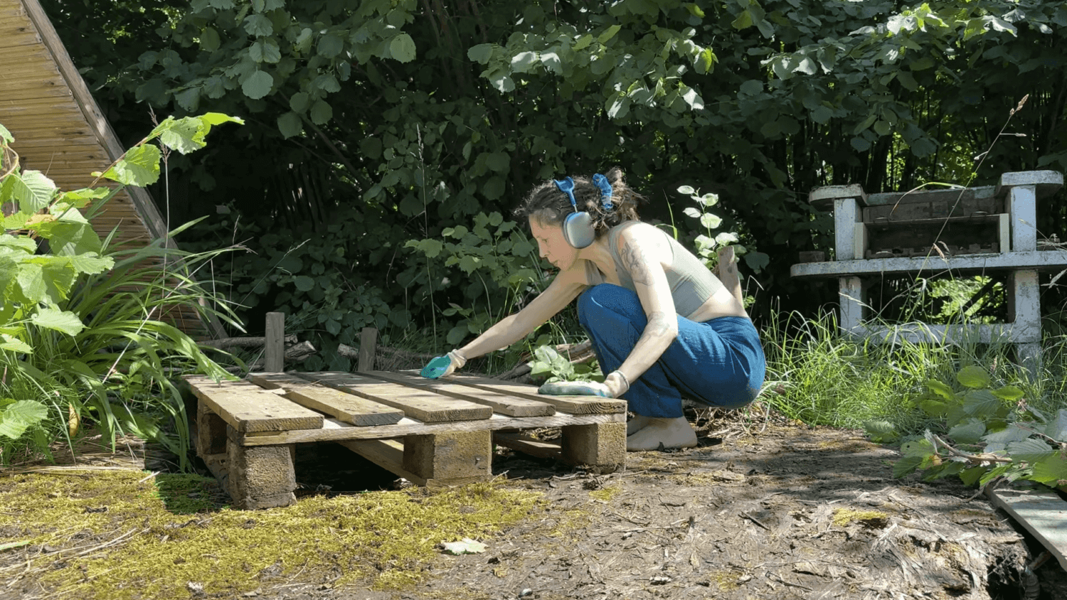 Kate kneels next to a pallete on a rotting terrace in the sun.