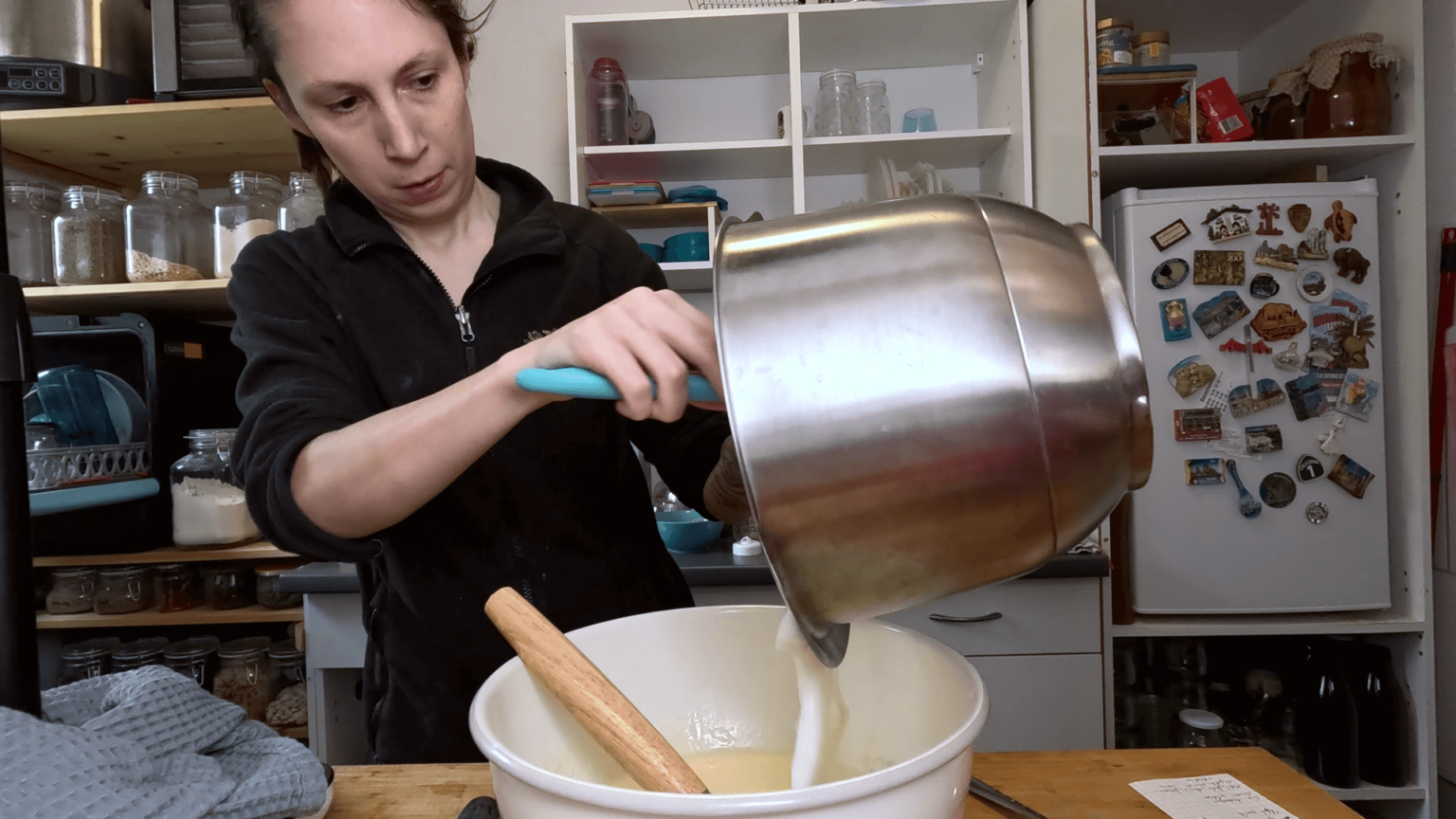 Kate holds a metal bowl and pours beaten egg white into another bowl.