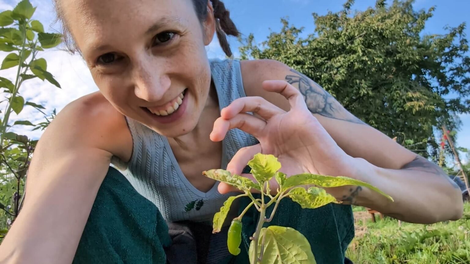 Kate is smiling into the camera while gently holding a leaf of a plant.