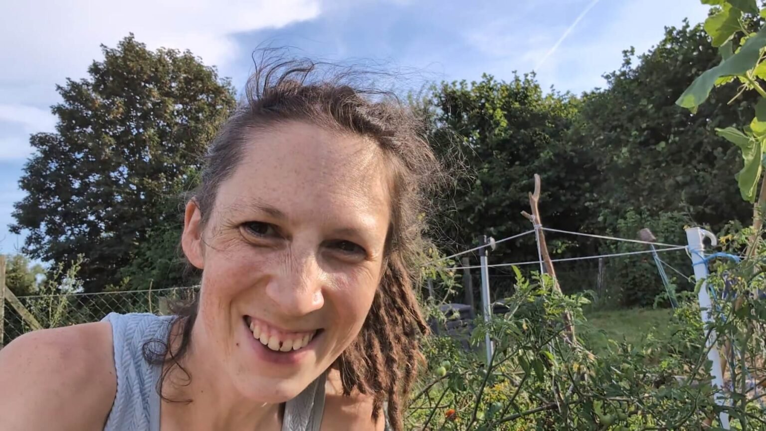 Kate is grinning next to her recovering tomato plants. She has something stuck between her front teeth.