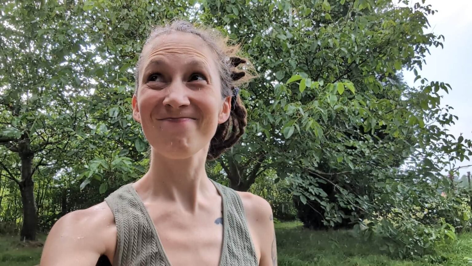 Kate is standign outside her garden house with the walnut and the cherry tree behind her. She is looking happy but annoyed because it is raining yet again.