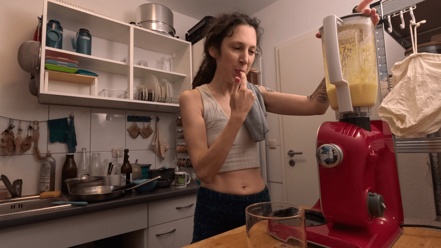 Kate is licking her finger. Her other hand rests on the blender with home-made mayonnaise. The counter behind her is full of dishes.