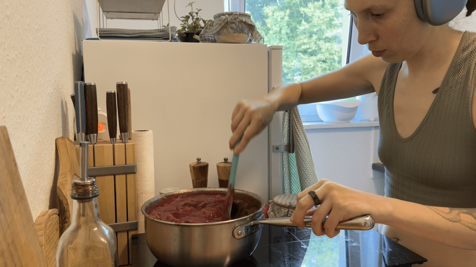 Kate stirrs a pot of plum butter. She is again wearing headphones.