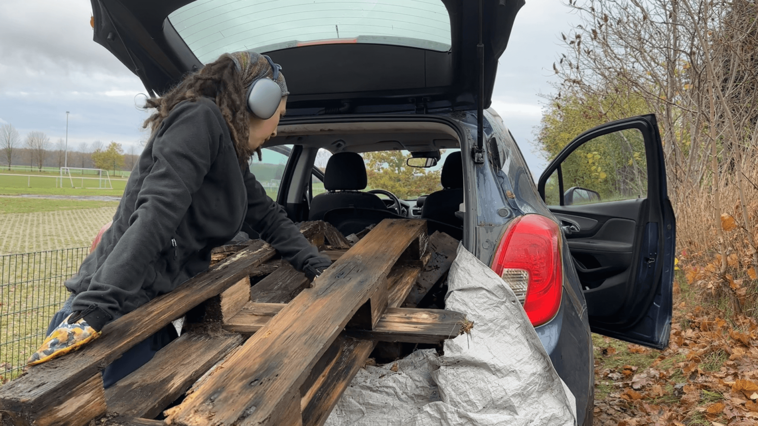 Kate pushes half a rotting pallet into her car. A tarp protects the trunk. Sh eis yet again wearing headphones.