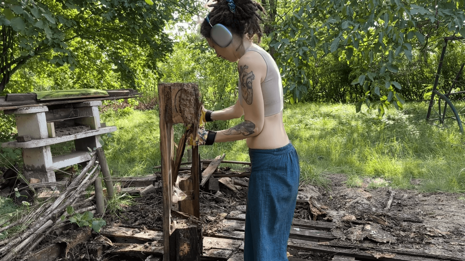 Kate stands in the middle of a former terrace built from palletes. She is lifting a half-rotten pallete.