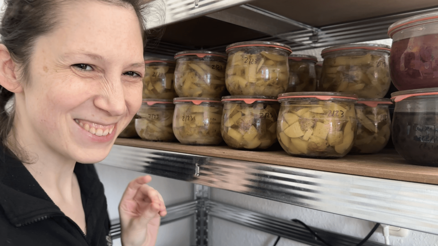 Kate grins next to a shelf with canned potatoes in jars.