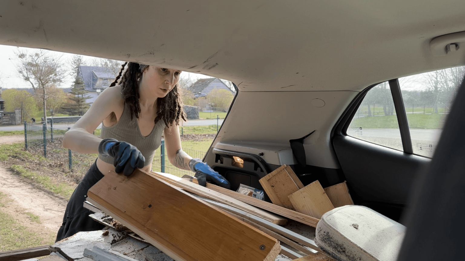 A view from inside the car out of the trunk where Kate is standing, pushing boards onto a growing pile in the trunk. The roof of her trunk is covered in darker stains.