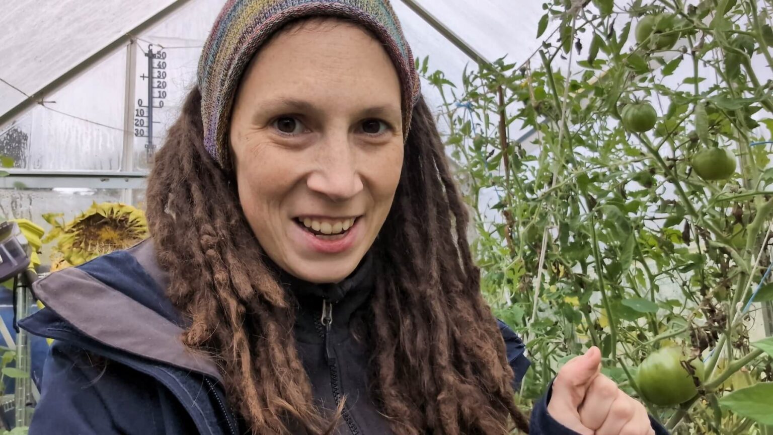 A portrait of Kate in front of her green tomatoes in the greenhouse.